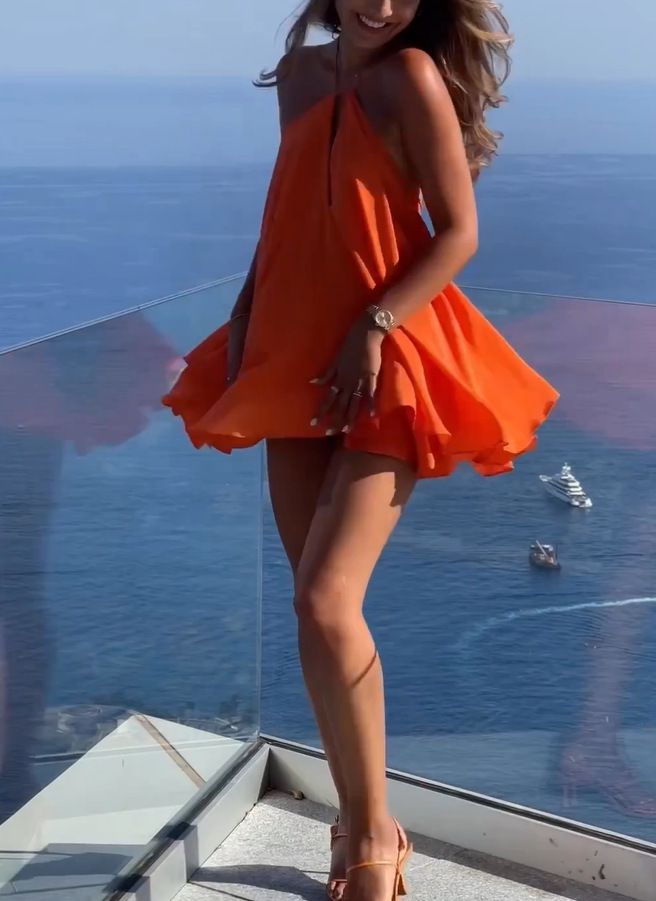 Woman in an orange dress standing on a balcony overlooking the ocean with boats.