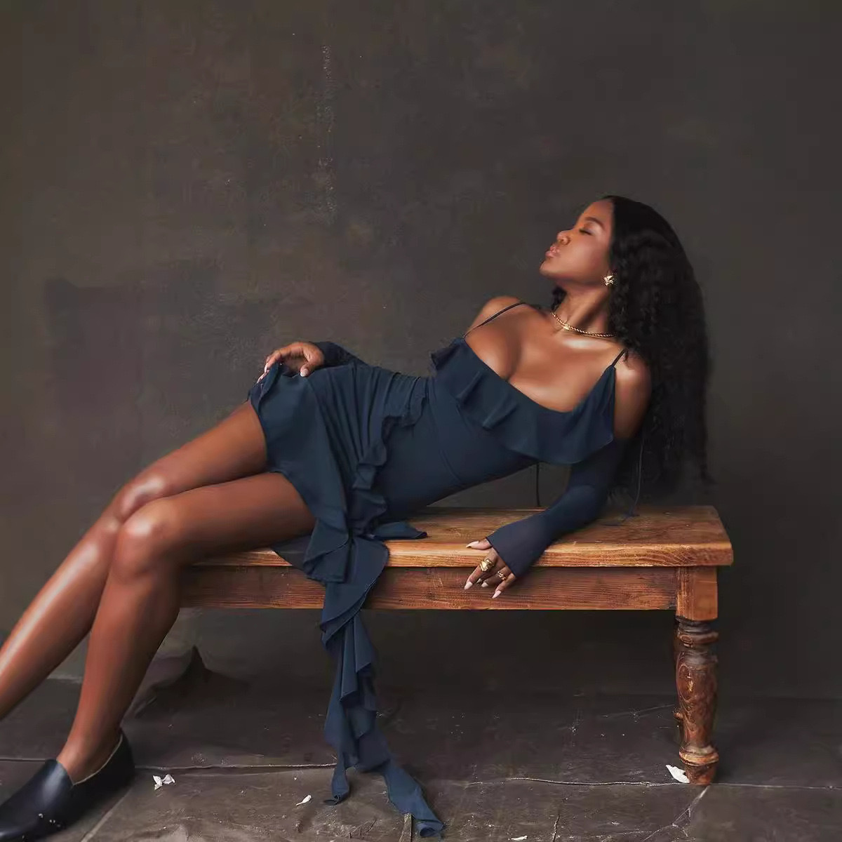 Woman in a blue dress sitting on a wooden bench against a dark background