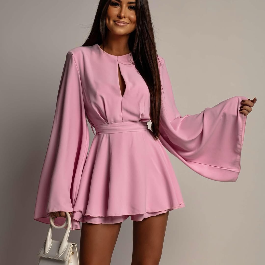 Woman wearing a pink dress with wide sleeves against a plain background