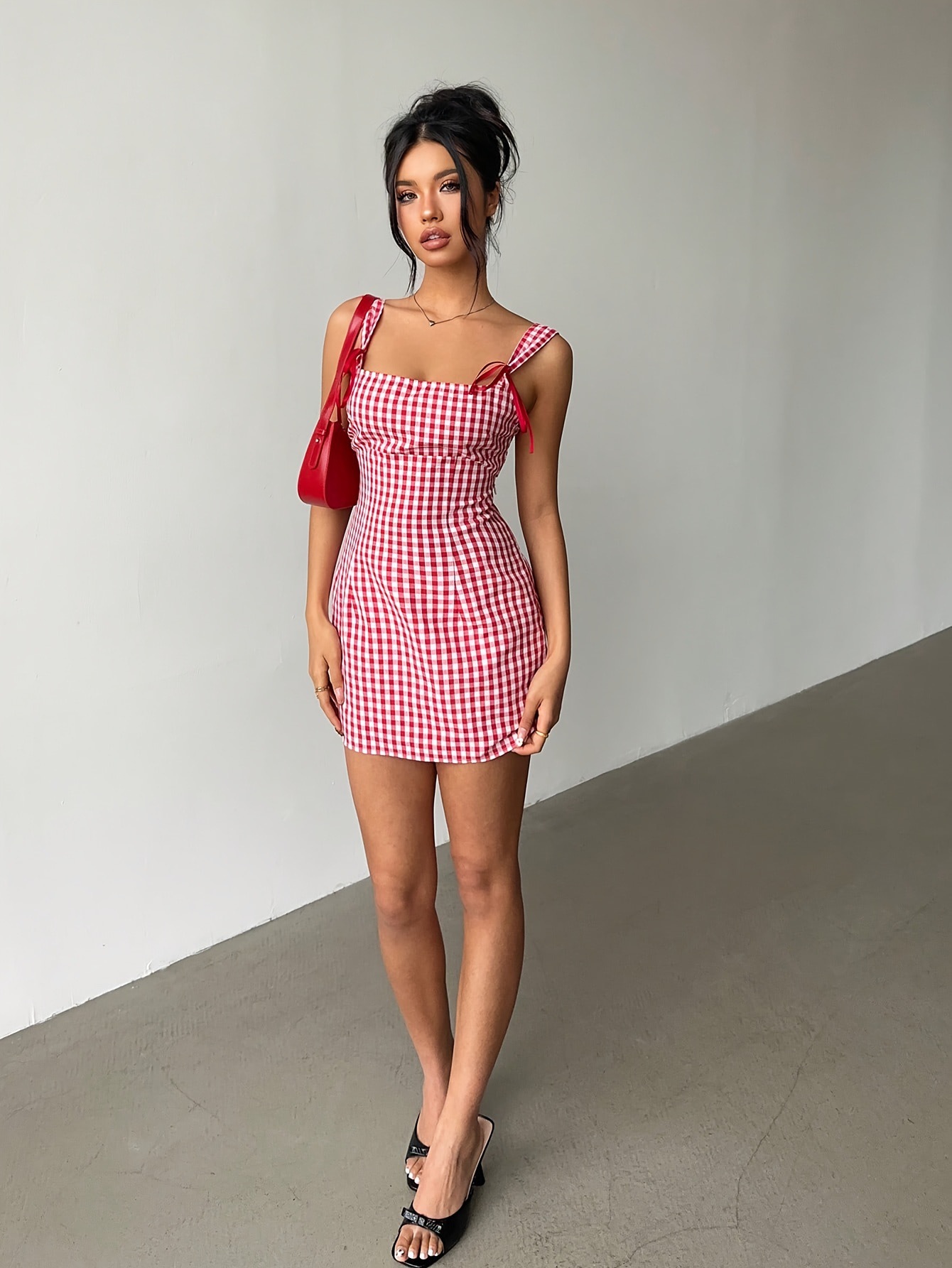 Woman wearing a red and white checkered dress with a red bag against a plain background
