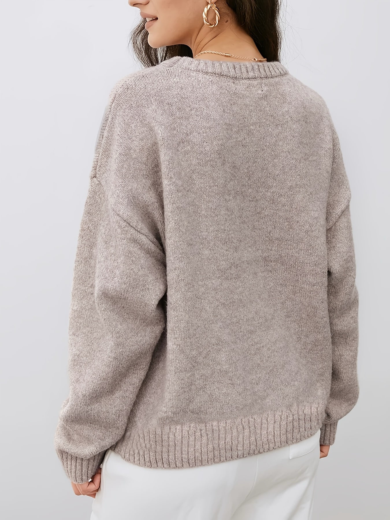 A woman wearing a light taupe knit sweater, shown from the back. The sweater has a soft, heathered texture and ribbed collar, cuffs, and hem, paired with white pants against a plain light gray background.