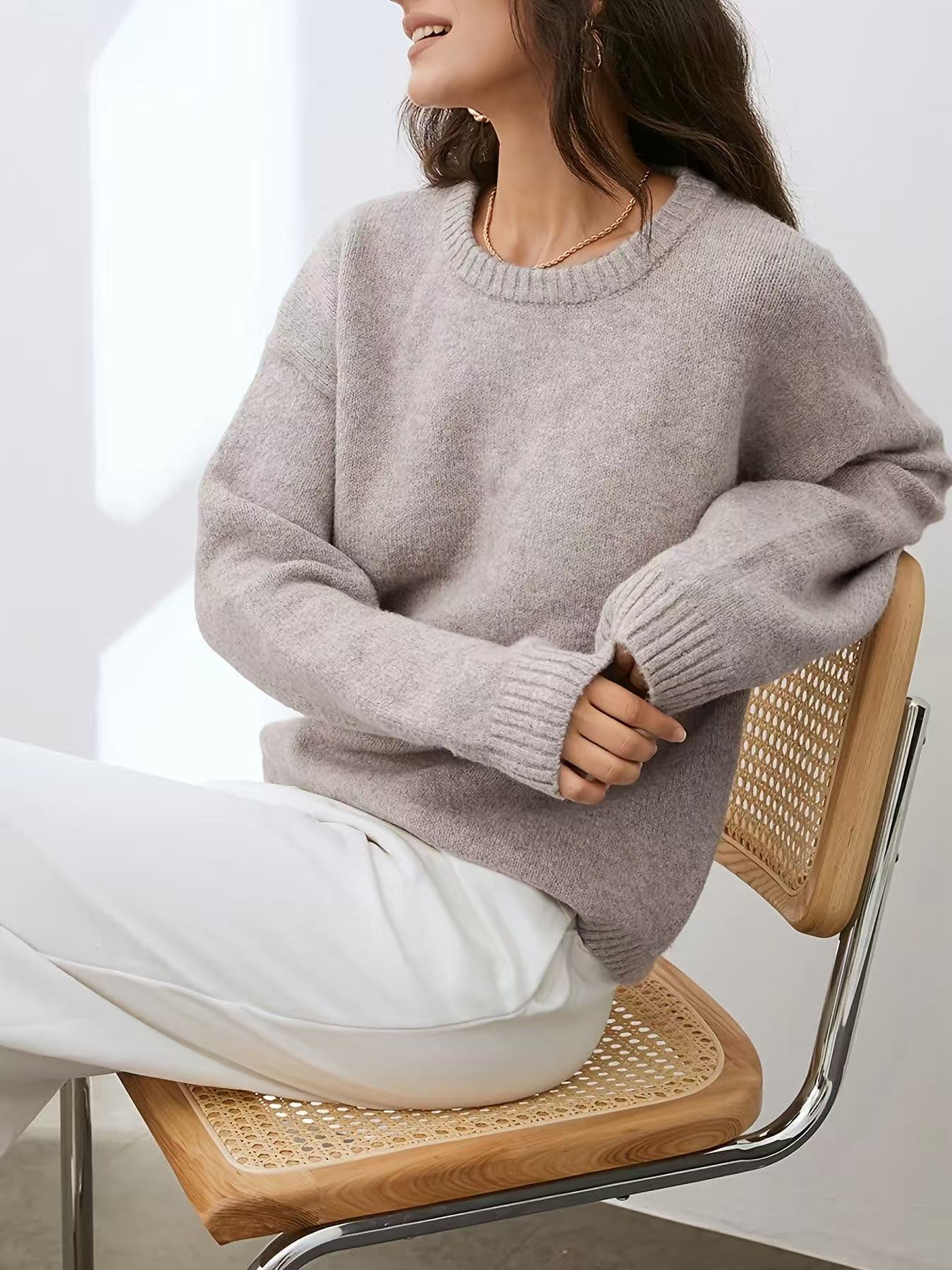 Person wearing a gray sweater and white pants sitting on a chair.