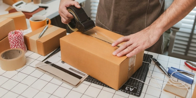 Dropshipping fulfillment worker packing taping cardboard shipping box tape dispenser