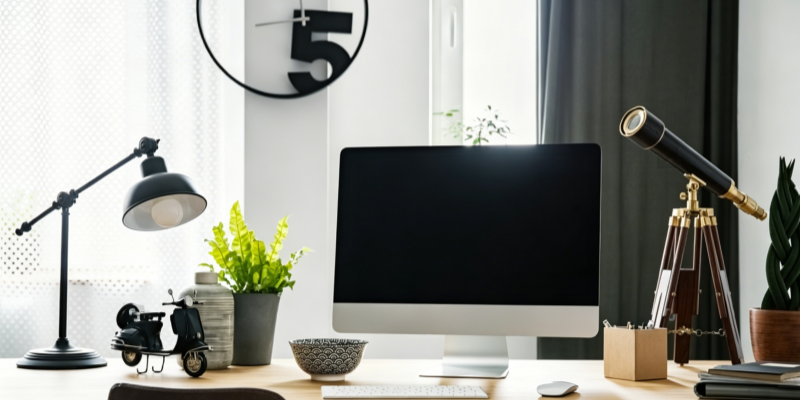 Modern home office desk setup with computer monitor desk lamp and telescope